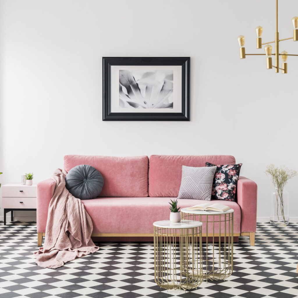 Poster above pink sofa in spacious living room interior with patterned armchair and plants. Real photo