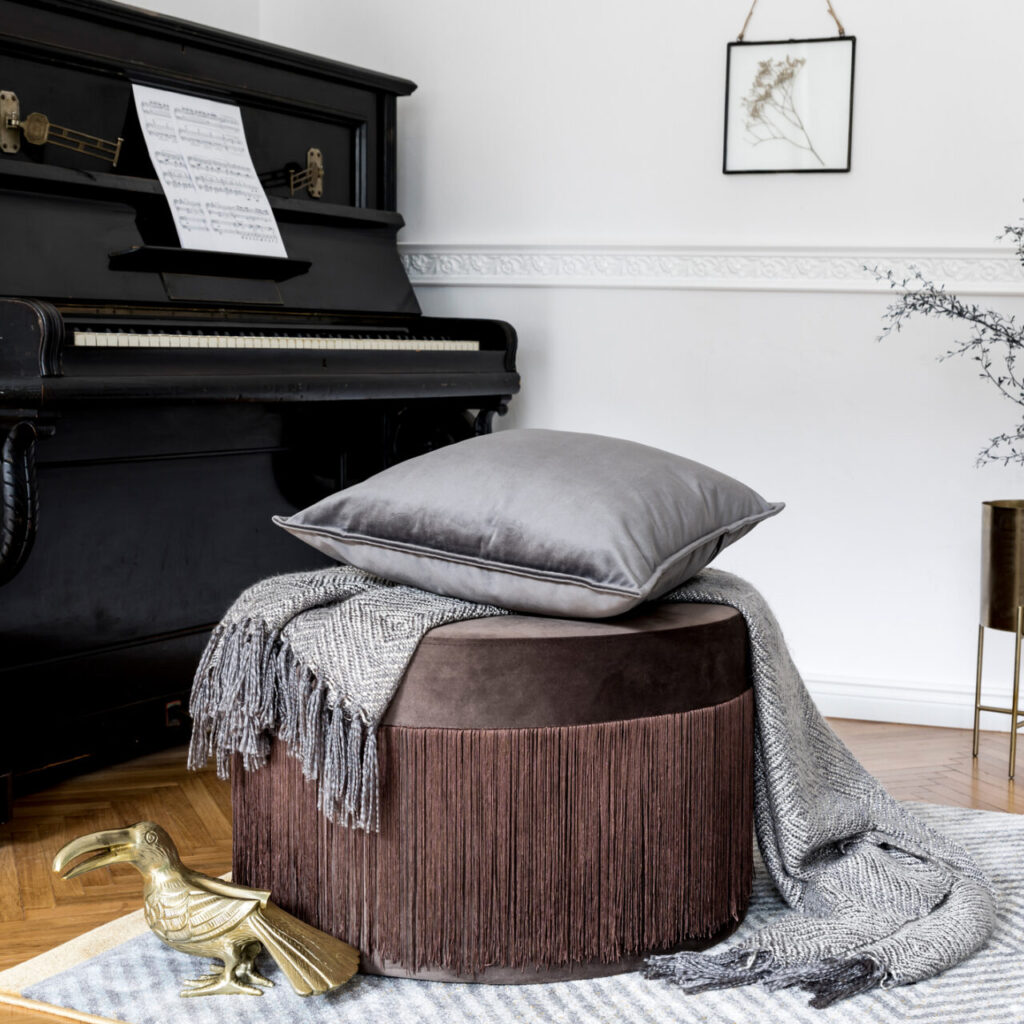 Stylish and luxury interior design of living room with brown velur pouf, pillows, plaid, sculpture, black piano, gold table, flowers and elegant personal accessories. Modern home decor. Template.