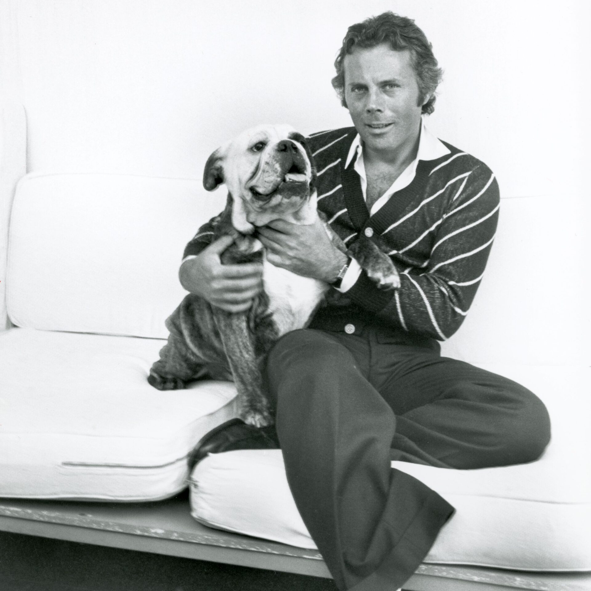 +Giorgio Armani sitting on a couch with his legs crossed and hugging a pet bulldog (Photo by Fairchild ArchivePenske Media via Getty Images) - GettyImages-1460915121