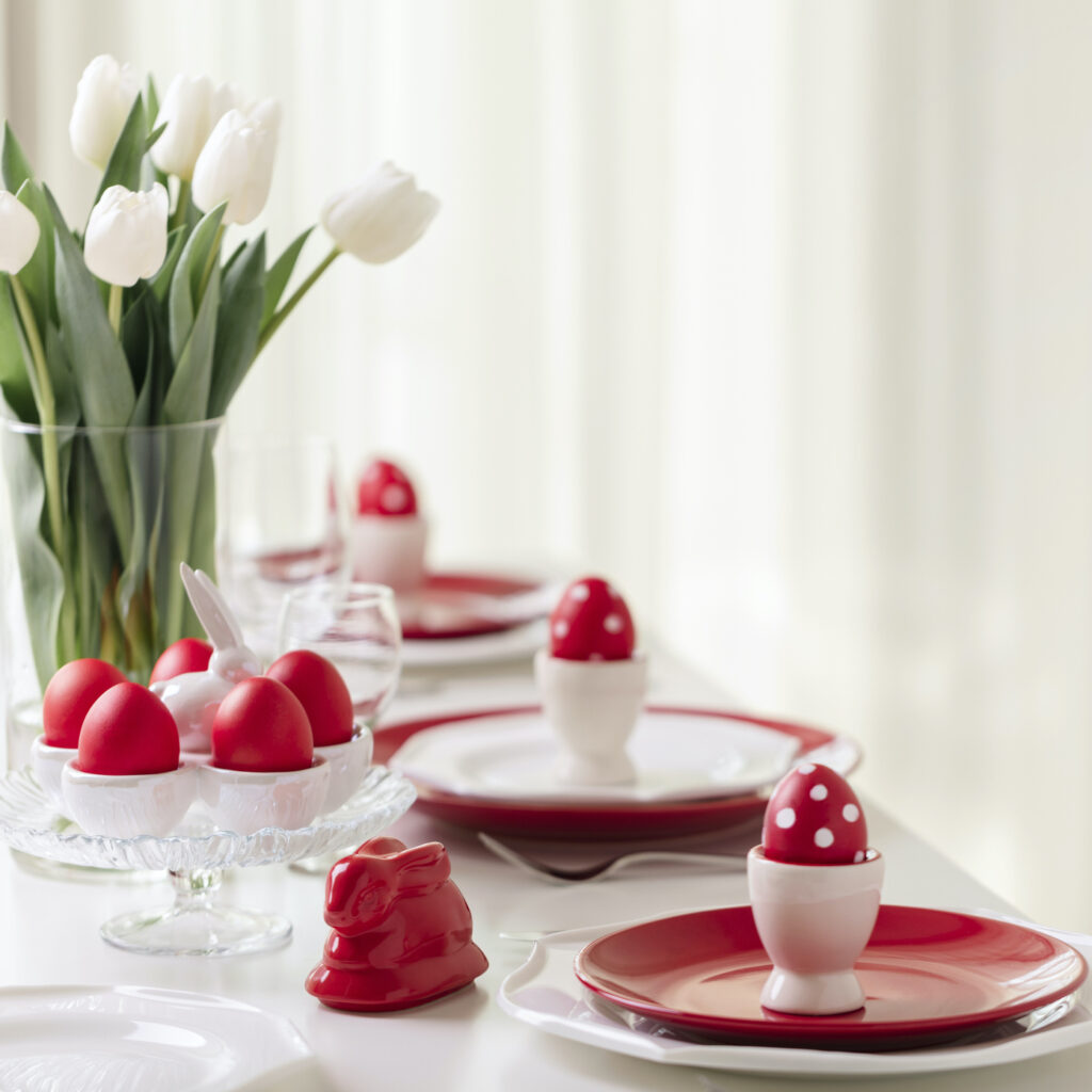 Happy easter. Decor and table setting of the Easter table is a vase with white tulips and dishes of red and white color. Easter colored eggs with white polka dots.